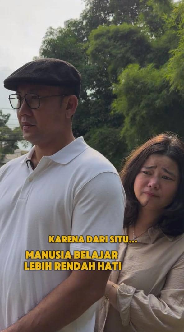 Seorang pria mengenakan kemeja putih dan topi hitam berdiri di samping seorang wanita berambut sebahu dengan latar pepohonan hijau.