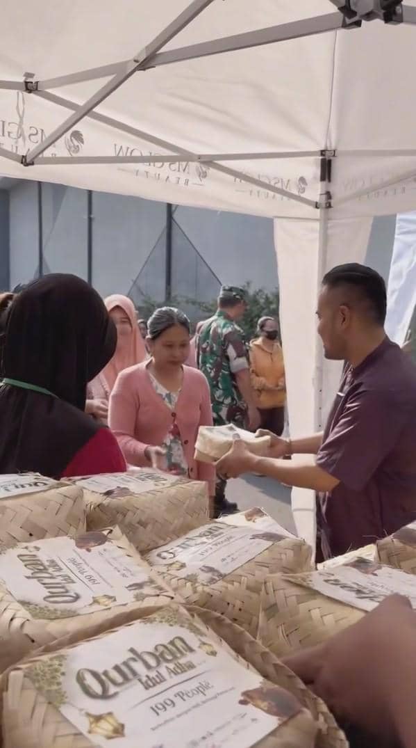 Seorang pria membagikan paket anyaman berisi daging kurban kepada warga yang antre di bawah tenda putih pada acara Idul Adha.