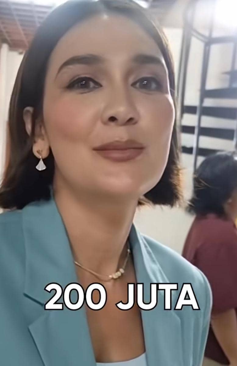 Seorang perempuan berambut pendek mengenakan blazer biru muda dan anting menjuntai dengan tulisan 200 juta di bagian bawah.