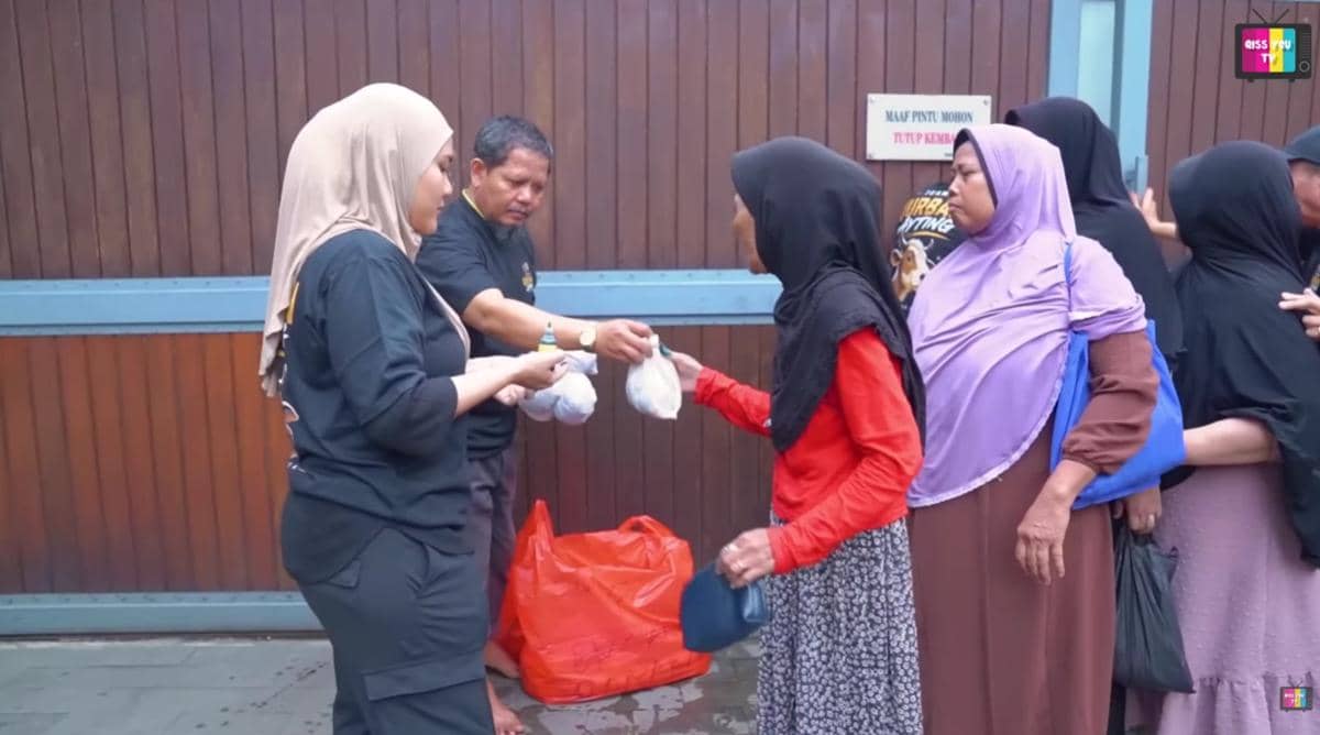 Beberapa orang membagikan daging kurban yang dibungkus plastik kepada warga yang antre di depan pagar kayu besar.