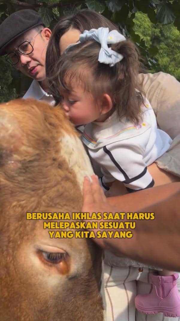 Seorang pria dan wanita bersama anak kecil mencium sapi kurban saat perayaan Idul Adha dengan suasana penuh kasih dan haru.