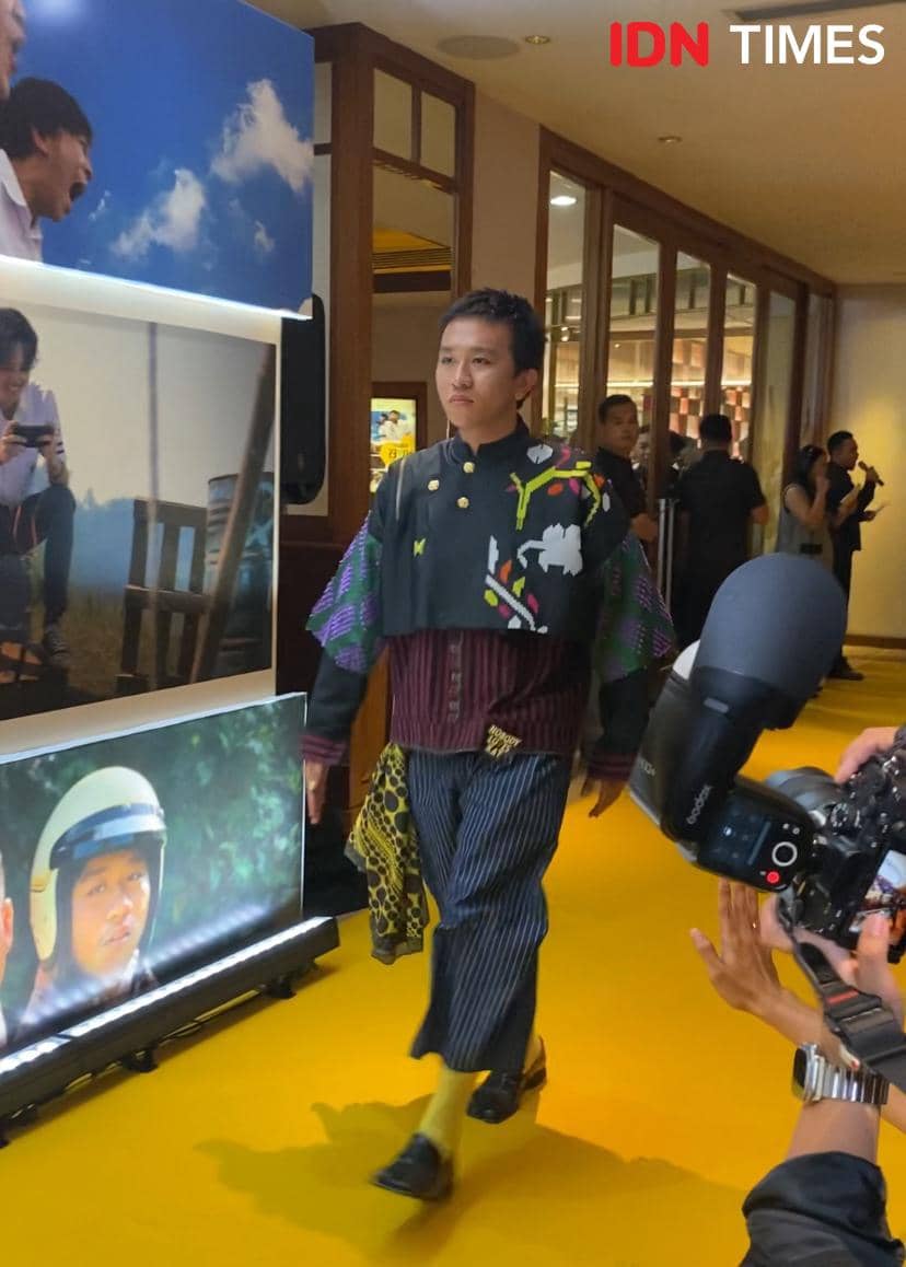 Seorang tamu berjalan di karpet kuning acara pemutaran film Nobody Loves Kay dengan busana unik bermotif warna-warni.