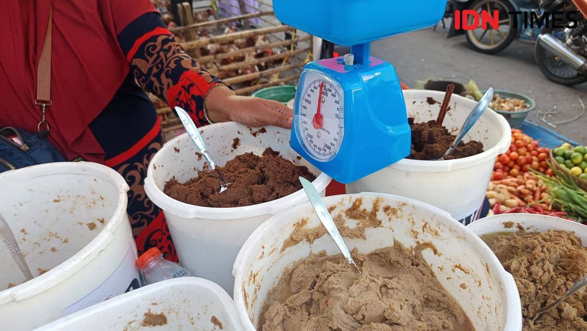 Penjual menimbang bumbu racik matang dalam ember putih di Pasar Pabaeng-baeng, Makassar, dengan timbangan biru di atas meja.