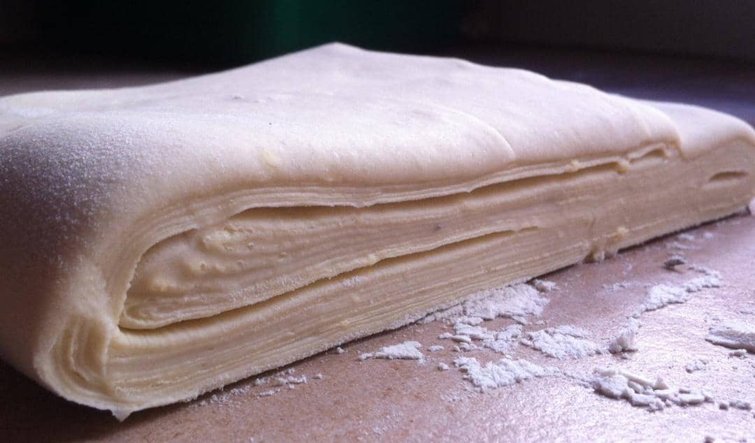 Lembaran kulit pastry berwarna kuning pucat dengan tekstur berlapis, siap digunakan untuk membuat aneka kue.