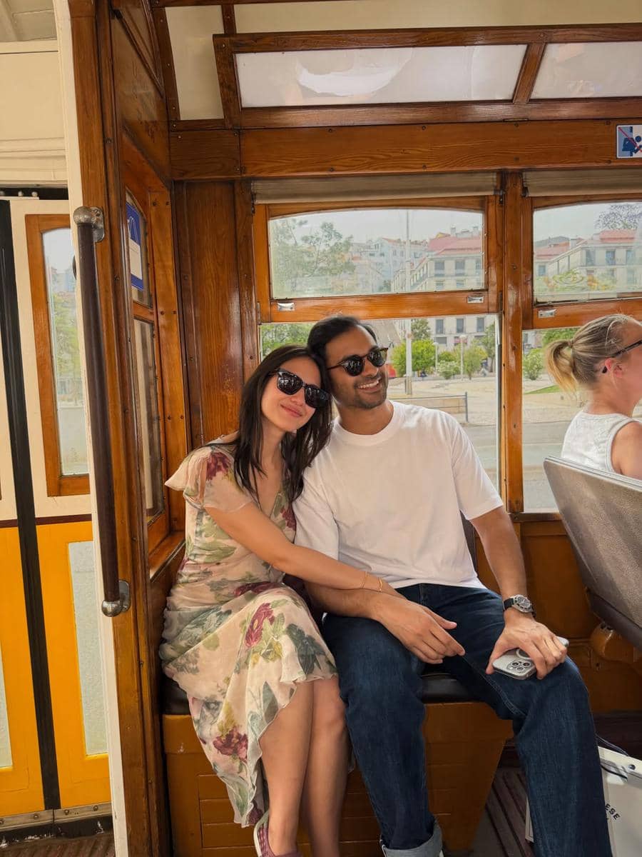 Seorang perempuan mengenakan gaun bermotif bunga duduk bersandar pada seorang pria di dalam trem kayu di Kota Lisbon.