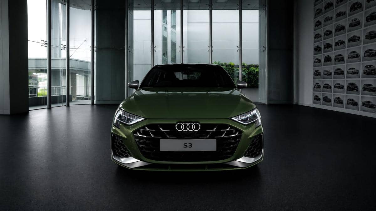 Mobil Audi S3 berwarna hijau District Green dipajang di ruang pamer modern dengan dinding kaca besar dan pencahayaan lembut.