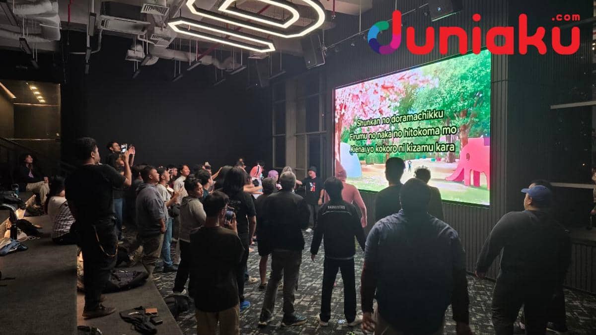 Sekelompok orang bernyanyi bersama di acara karaoke Warga di The Plaza, IDN HQ, dengan layar besar menampilkan lirik lagu.