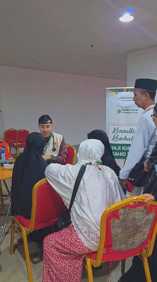 Seorang tenaga medis berbicara dengan beberapa calon jemaah haji yang duduk di kursi saat konsultasi kesehatan di sebuah ruangan.