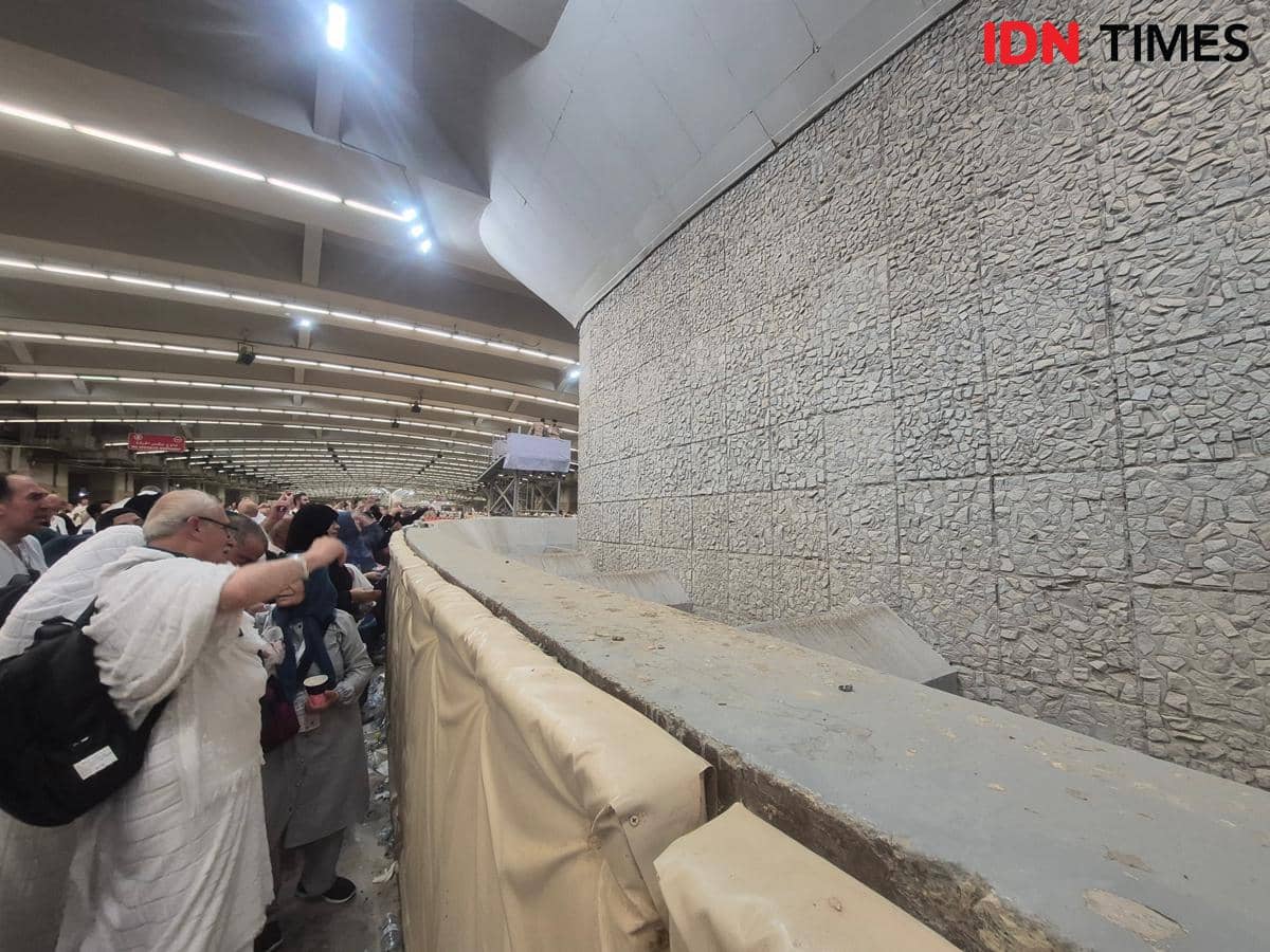 Jemaah haji mengenakan pakaian ihram sedang melontar jumrah aqabah di area Jamarat pada dini hari dengan suasana ramai dan tertib.