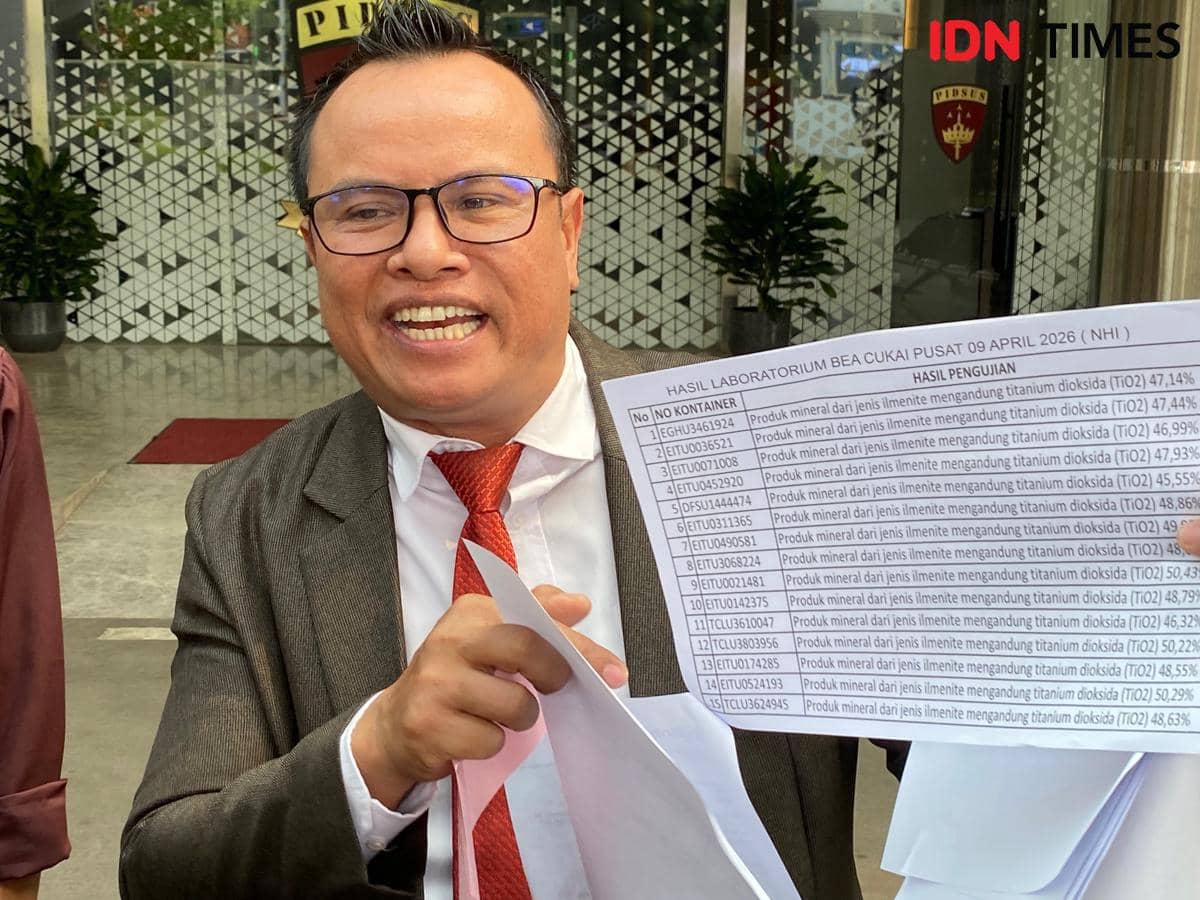 Seorang pria mengenakan jas abu-abu dan dasi merah memegang lembar hasil laboratorium bea cukai bertuliskan data uji mineral di luar gedung.