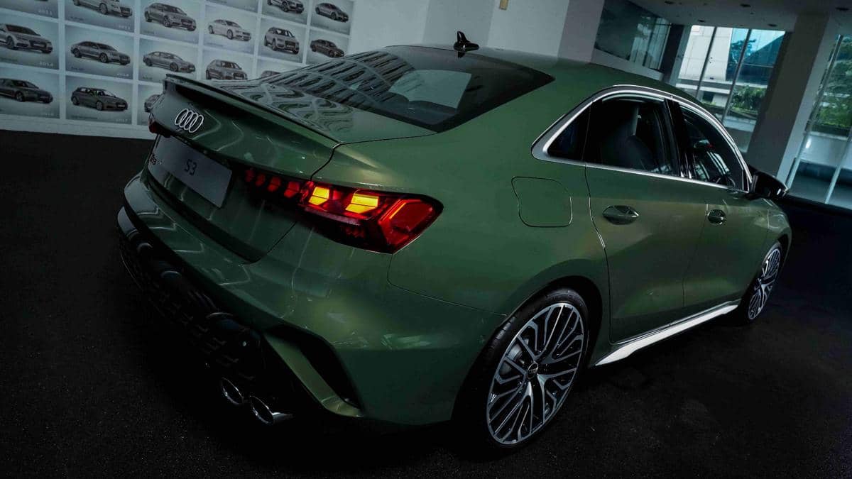 Mobil sedan Audi S3 berwarna hijau tampak dari sisi belakang dengan lampu belakang menyala di ruang pameran.