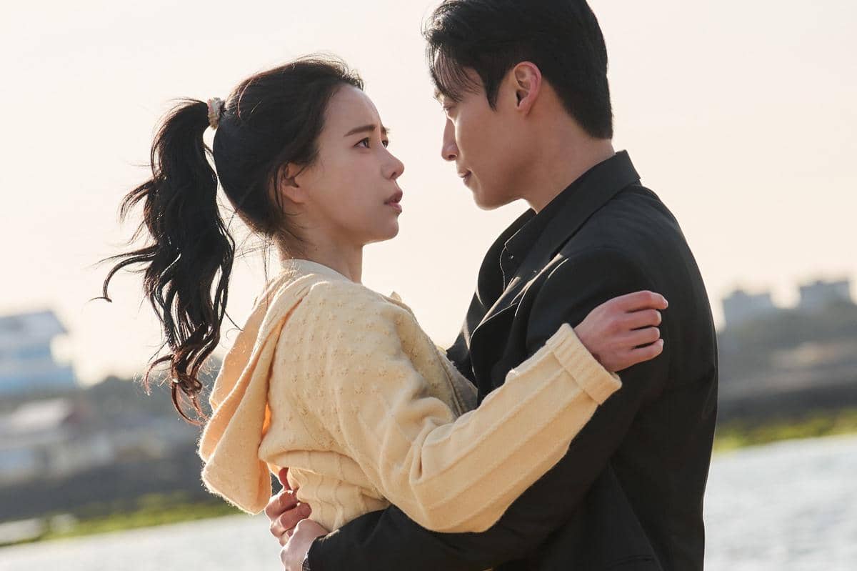 Dua karakter dalam drama My Royal Nemesis saling menatap intens di tepi pantai, dengan suasana romantis dan emosional.