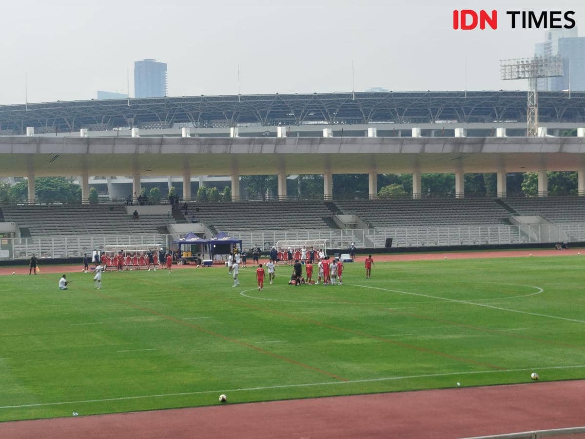 Pemain Timnas Indonesia berlatih di Stadion Madya dengan latar tribun kosong dan gedung tinggi di kejauhan.