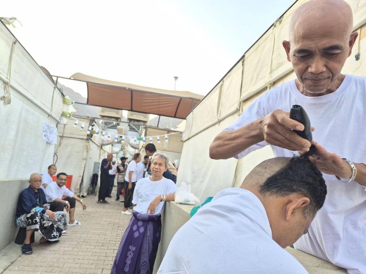 Seorang jemaah haji mencukur rambut seorang pria hingga gundul di area terbuka sebagai bagian dari prosesi tahalul setelah ibadah haji.