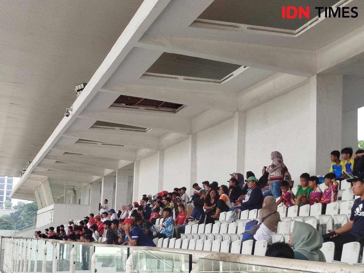 Penonton duduk di tribun Stadion Madya menyaksikan latihan Timnas Indonesia dengan suasana ramai dan antusias.