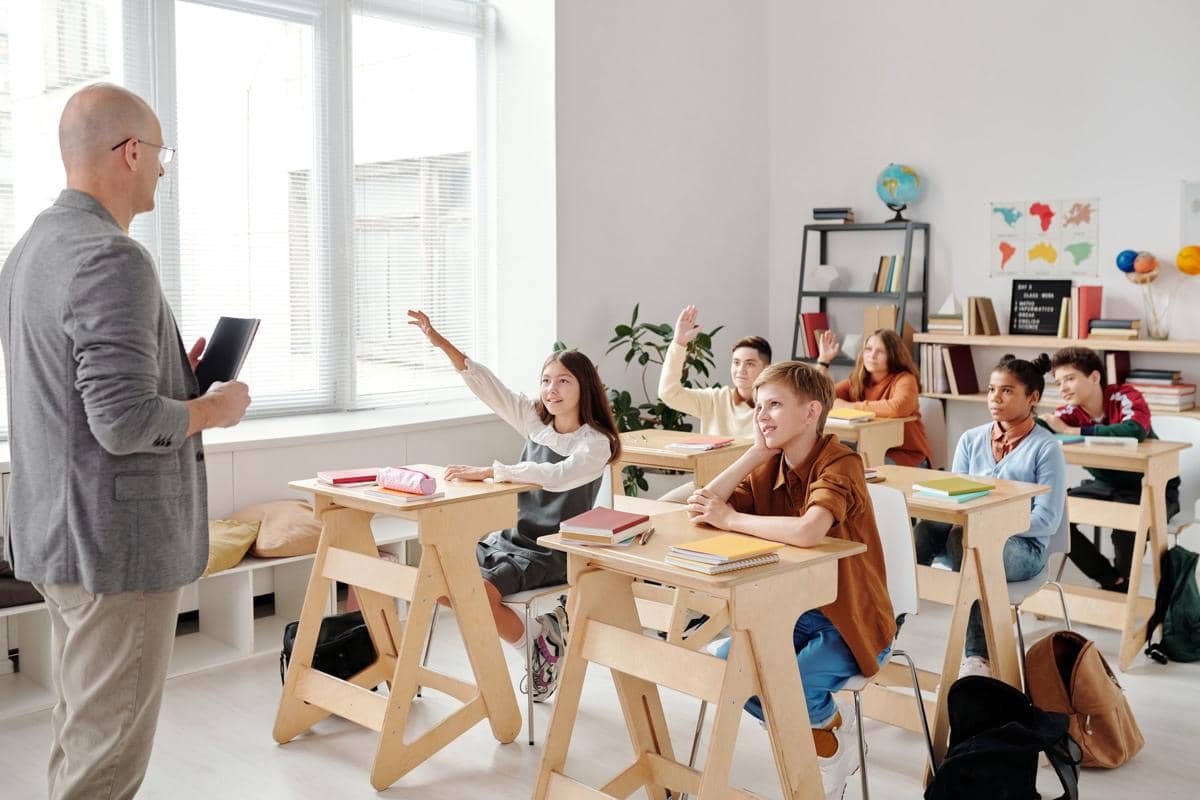 Suasana guru sedang mengajar di depan murid-murid di dalam kelas.