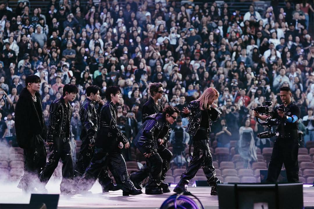 Grup musik tampil di atas panggung dengan busana hitam serasi di depan penonton yang memenuhi stadion selama tur Arirang.