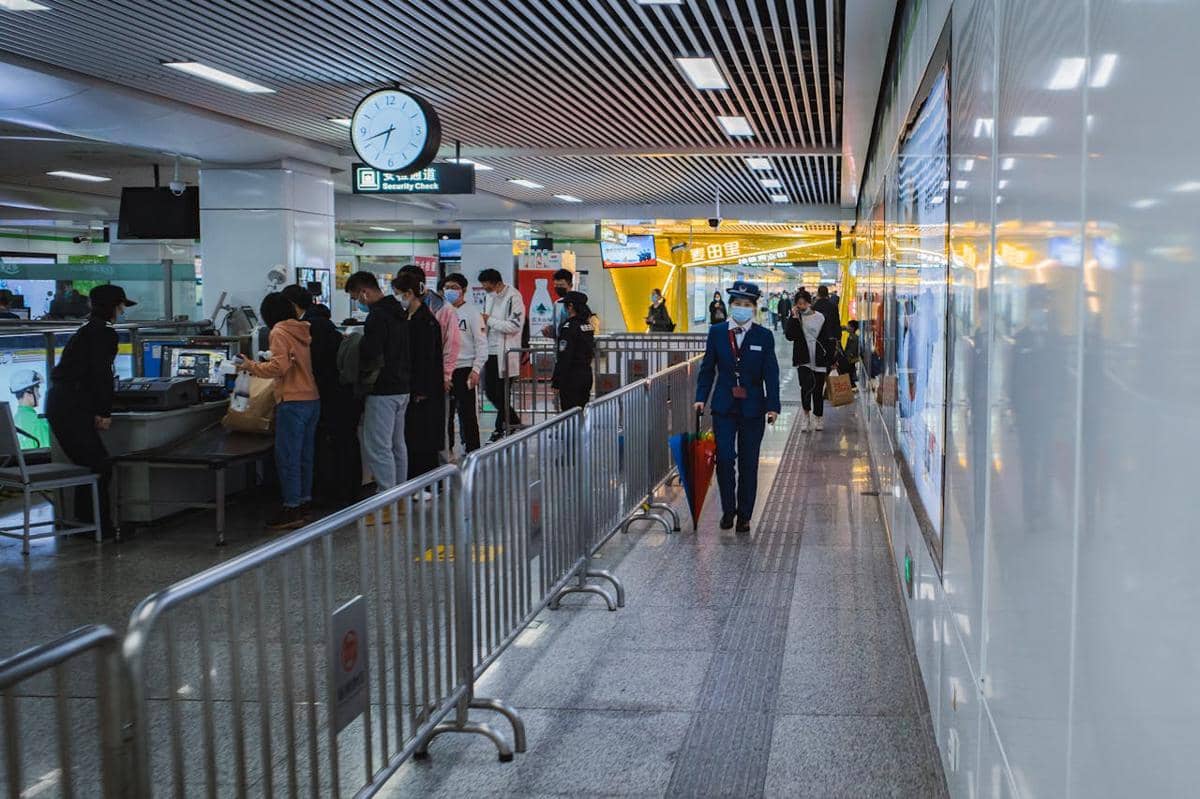 Penumpang antre di area pemeriksaan keamanan bandara internasional dengan petugas dan suasana terminal yang ramai.