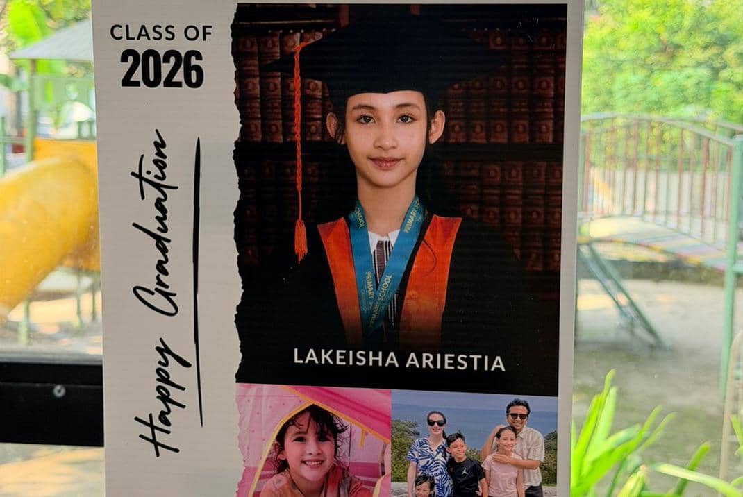 Seorang anak mengenakan toga dan medali kelulusan dengan tulisan Class of 2026 serta kolase foto keluarga di bagian bawah.