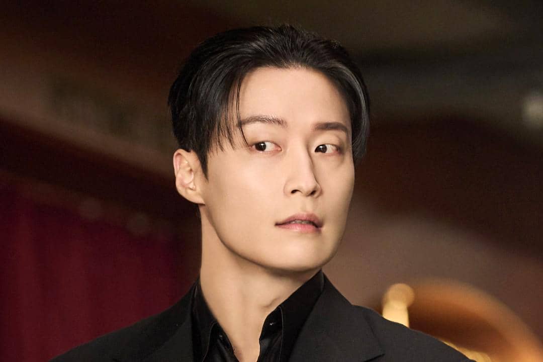 Seorang pria berpenampilan rapi mengenakan setelan hitam dengan ekspresi serius dalam cuplikan drama My Royal Nemesis.