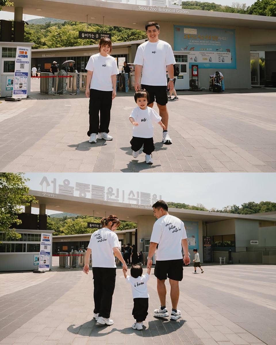 Sebuah keluarga mengenakan kaus putih dan celana hitam berjalan bersama anak kecil di depan gerbang Seoul Zoo Botanical Garden.