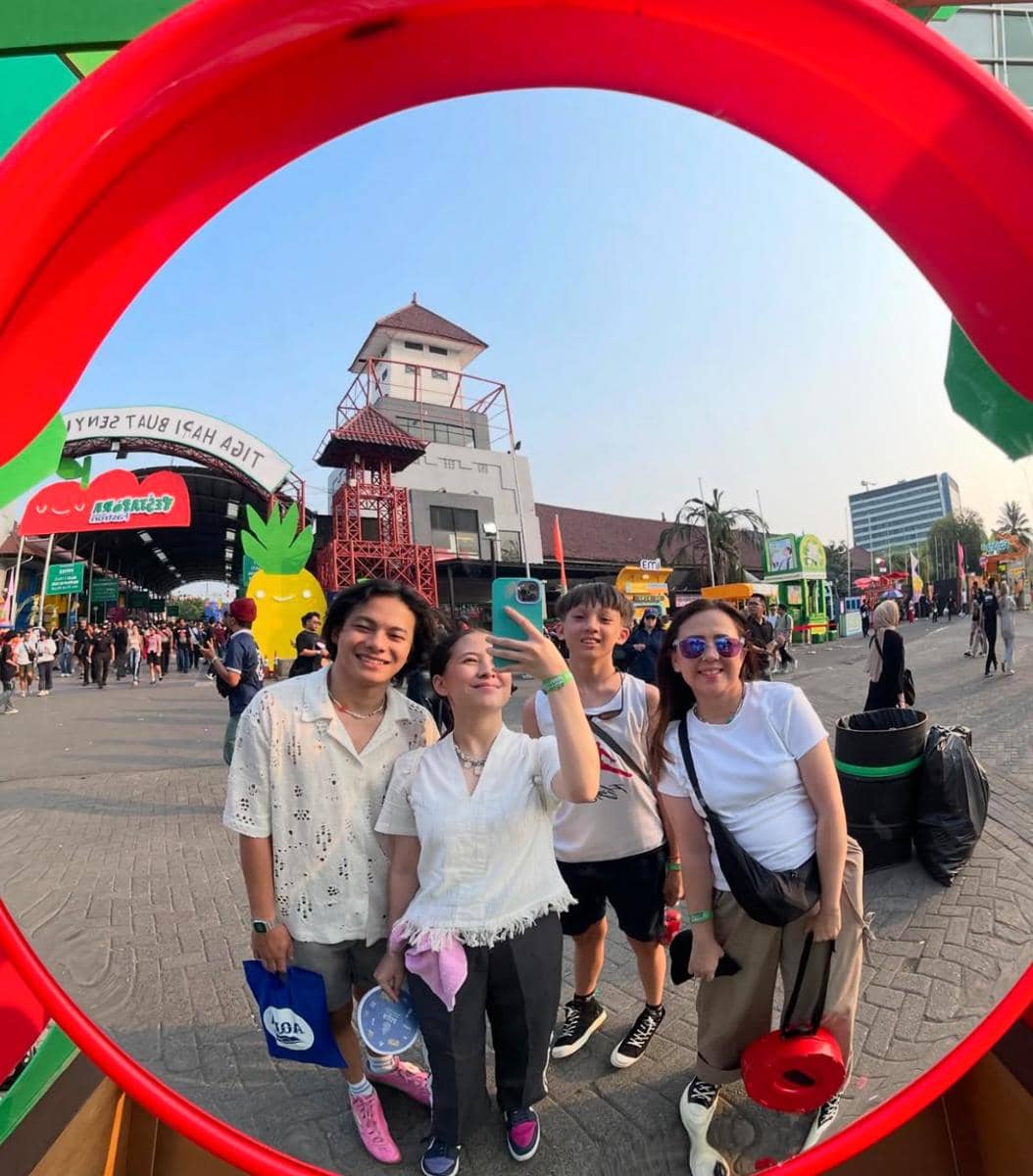 Empat orang berpose bersama sambil berfoto di cermin bundar di area luar wahana hiburan dengan suasana ramai dan cerah.