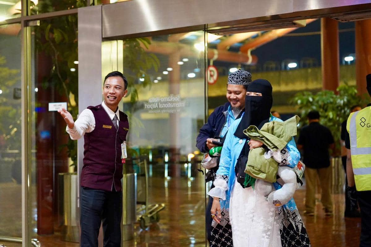 Petugas bandara membantu sepasang jemaah haji yang tiba di Bandara Soekarno-Hatta dengan suasana malam hari di area kedatangan.