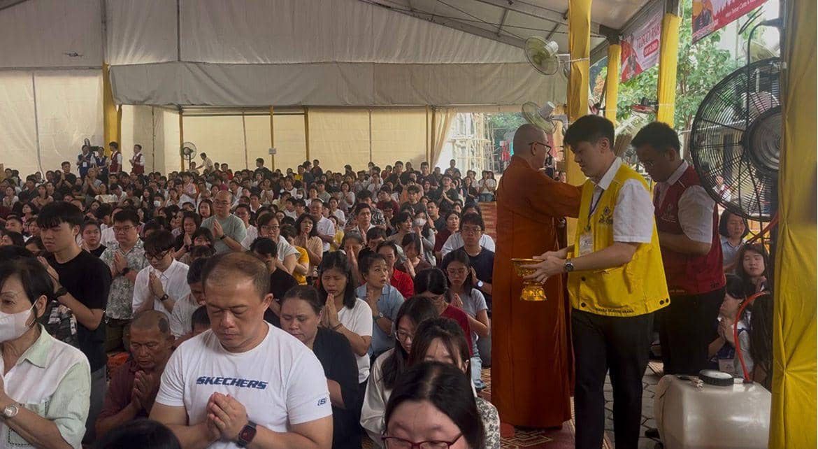 Umat Buddha berkumpul dalam doa bersama saat perayaan Waisak di sebuah tenda besar, dipimpin oleh biksu dan panitia berpakaian seragam.