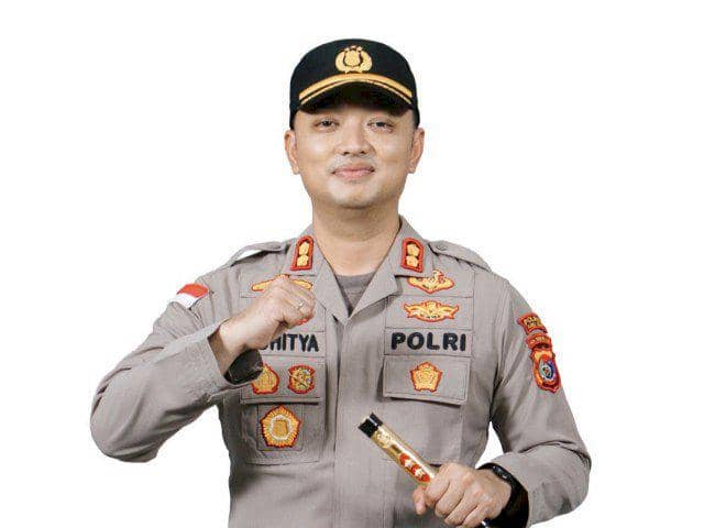 Seorang perwira polisi mengenakan seragam lengkap dengan topi dan atribut kepolisian, berpose dengan tangan mengepal di dada.