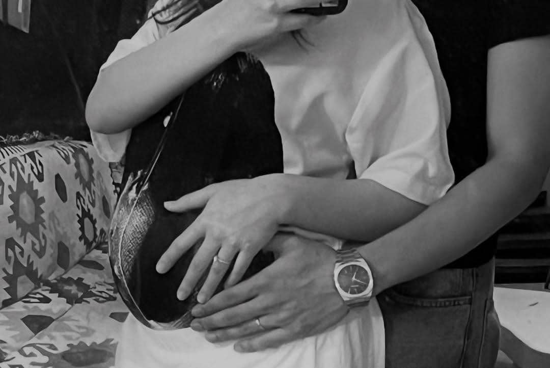Sepasang pria dan wanita berpelukan erat sambil memperlihatkan cincin di jari manis mereka dalam suasana hangat hitam putih.