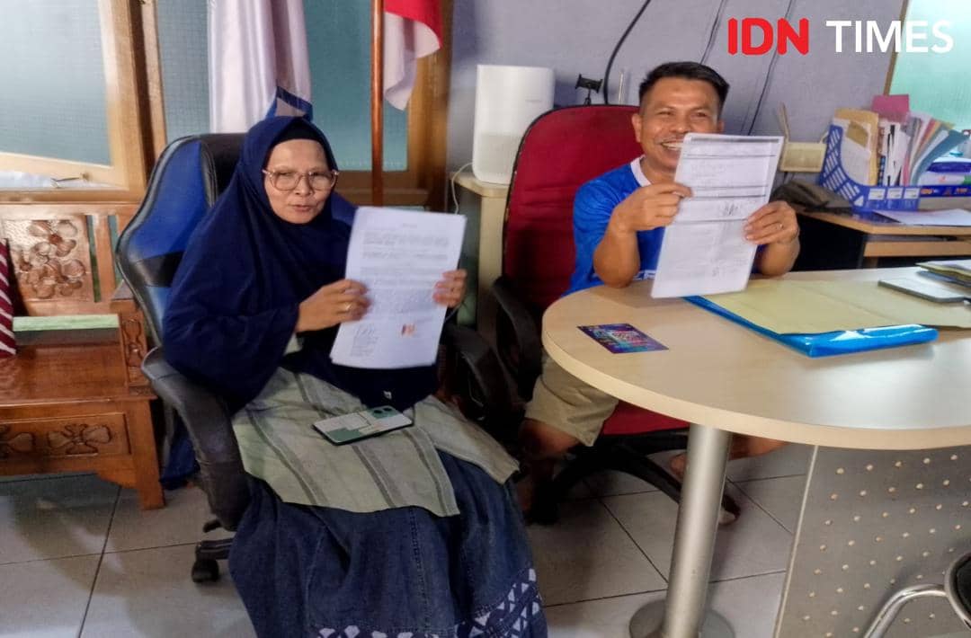 Seorang perempuan berhijab dan seorang pria duduk di kantor sambil memegang dokumen pengaduan di Purwokerto.
