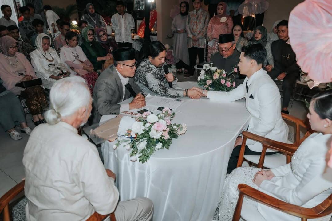 Suasana akad nikah dengan pengantin pria berjabat tangan dengan wali di depan saksi dan tamu yang mengenakan busana formal.