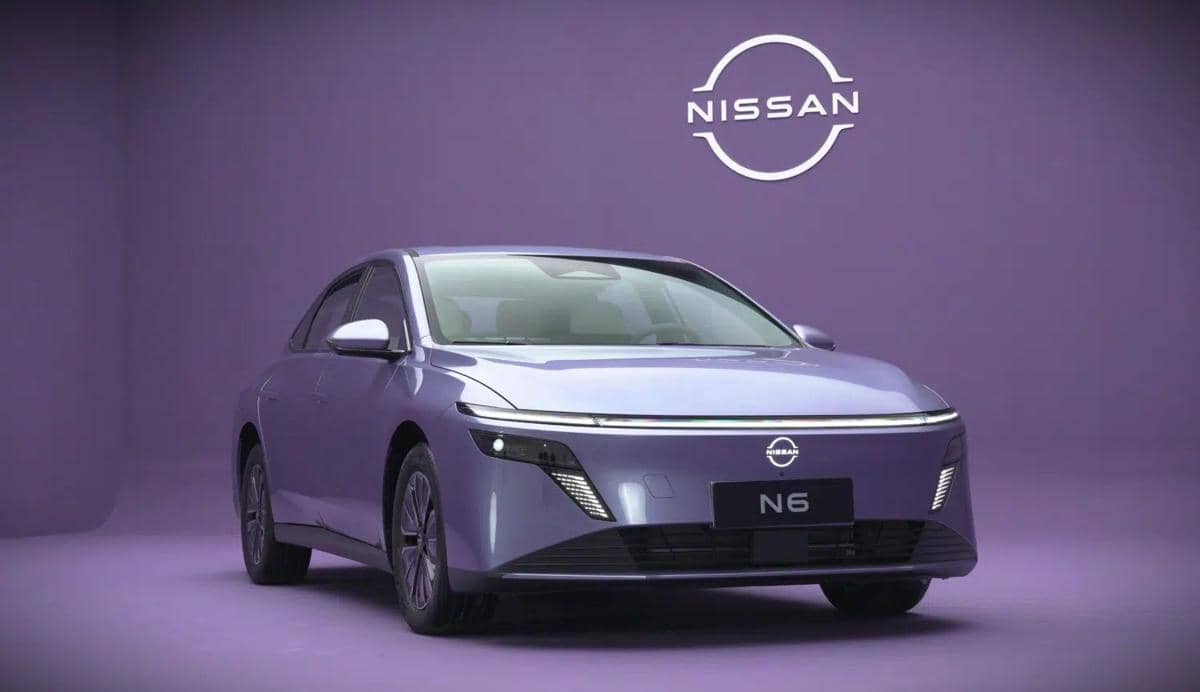 Mobil listrik Nissan N6 berwarna ungu dipamerkan di studio dengan latar belakang ungu dan logo Nissan di dinding belakang.