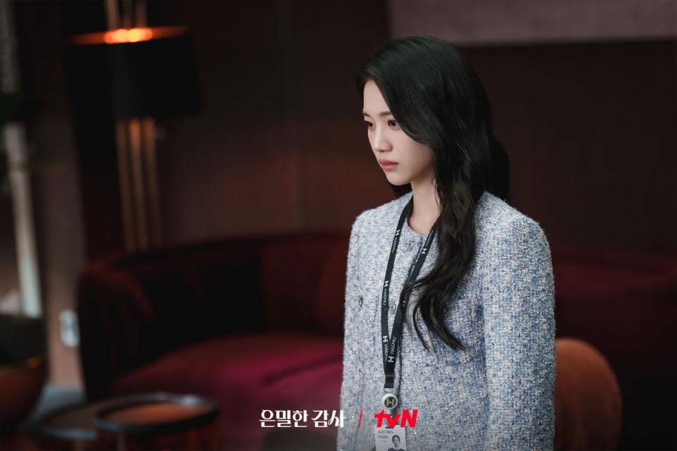 Seorang wanita berambut panjang mengenakan blazer biru muda berdiri di ruangan dengan sofa merah marun dalam cuplikan drama Korea Filing for Love.