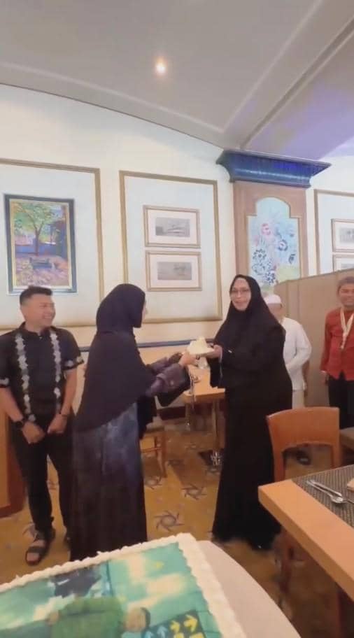Pasangan mengenakan busana hitam merayakan hari jadi pernikahan di sebuah ruangan dengan kue besar di atas meja.