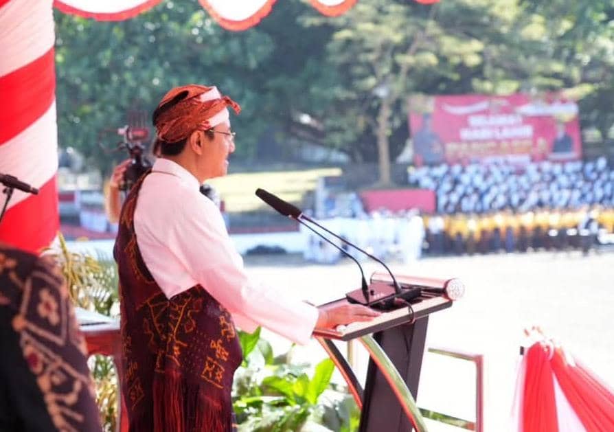 Seorang pria mengenakan pakaian adat berbicara di podium pada perayaan Hari Lahir Pancasila di Ende dengan latar peserta upacara.