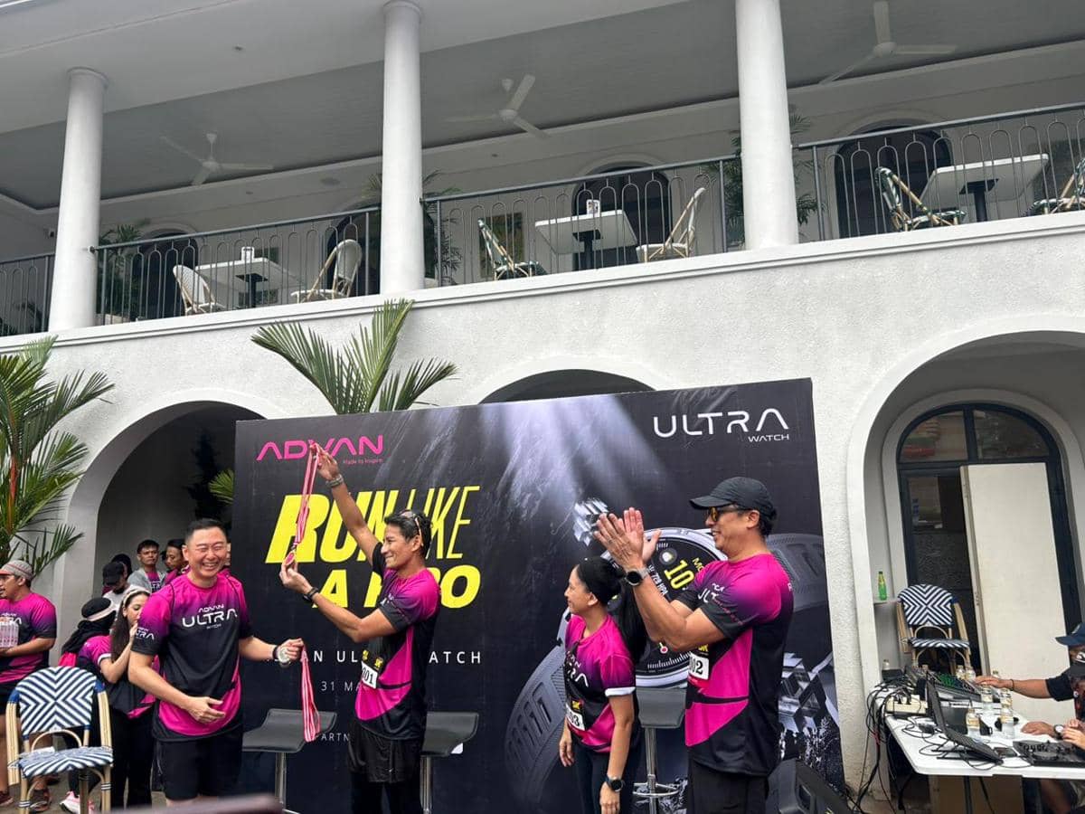 Beberapa peserta mengenakan kaus ungu hitam acara Advan Run Like a Pro berpose di depan backdrop bertuliskan Ultra Watch di area luar gedung.
