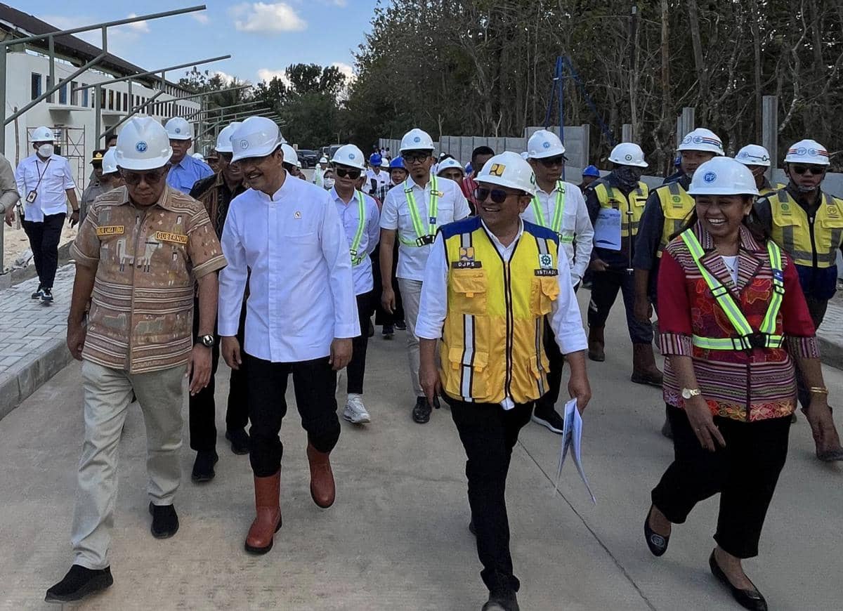 Rombongan pejabat mengenakan helm proyek meninjau pembangunan gedung Sekolah Rakyat di Nusa Tenggara Timur pada siang hari.