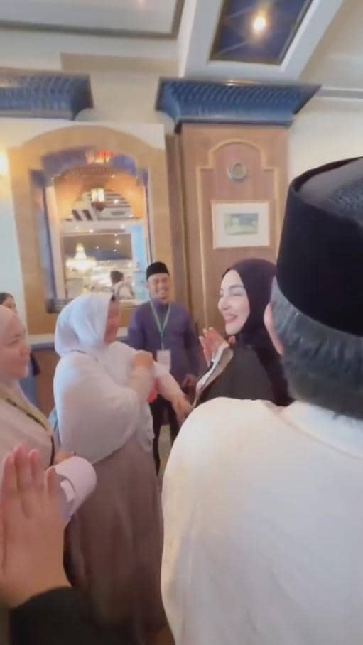 Beberapa orang berpakaian muslim saling berjabat tangan dan tersenyum di dalam ruangan dengan dekorasi elegan bernuansa hangat.