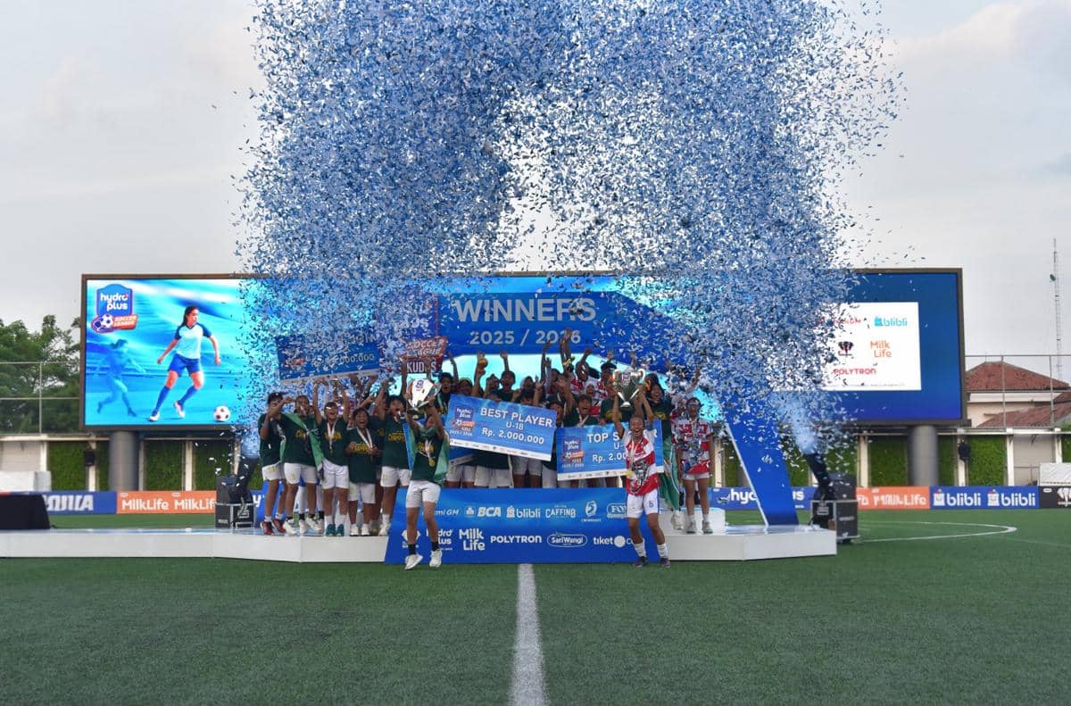 Para pemain sepak bola merayakan kemenangan di panggung juara Hydroplus Soccer League Kudus dengan confetti biru berhamburan di udara.