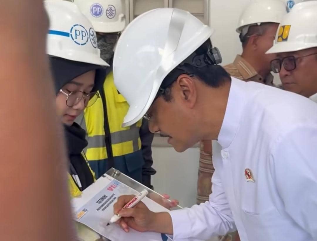 Seorang pejabat mengenakan helm proyek putih meninjau pembangunan gedung sekolah bersama tim konstruksi di Nusa Tenggara Timur.