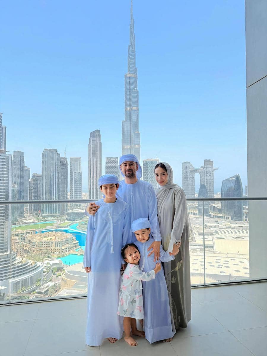 Sebuah keluarga berpose di balkon dengan latar gedung pencakar langit Burj Khalifa di Dubai pada siang hari yang cerah.