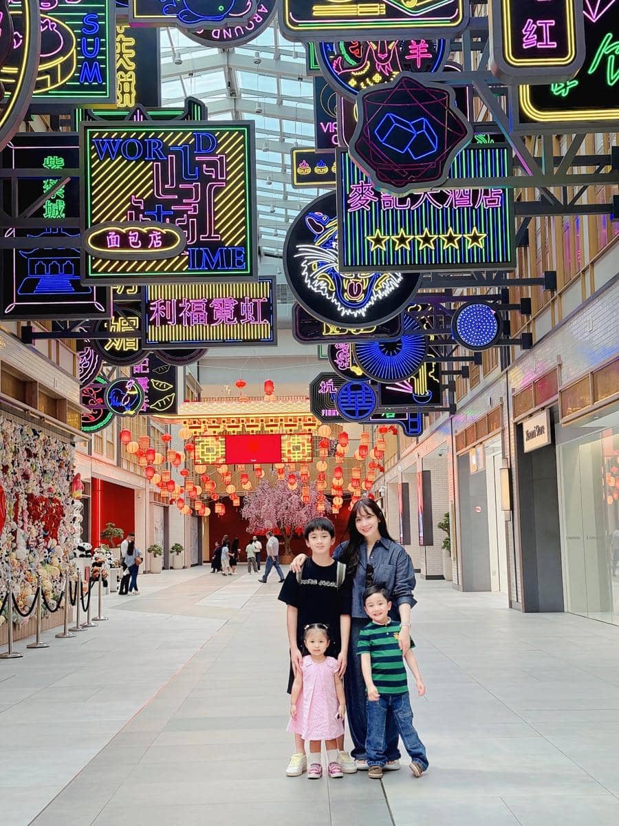 Seorang wanita bersama tiga anak berpose di koridor pusat perbelanjaan dengan dekorasi lampu neon warna-warni dan lentera merah di Dubai.