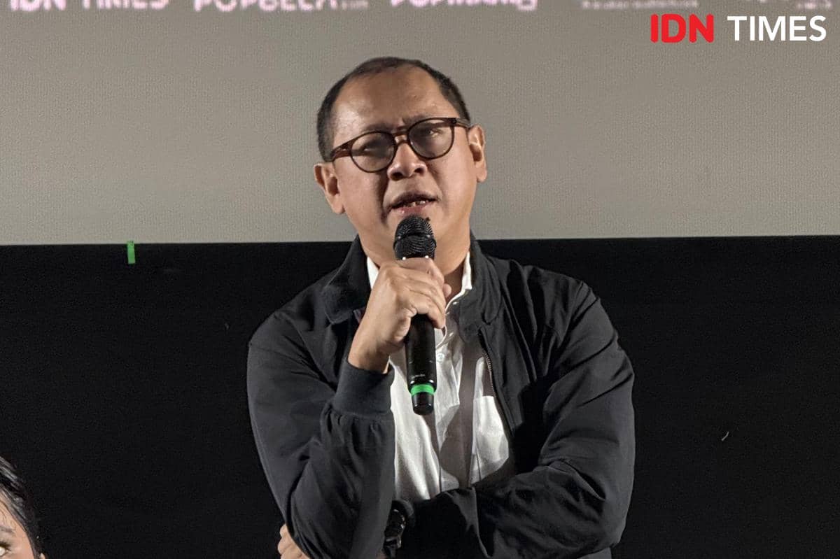 Seorang pria mengenakan kacamata dan jaket hitam memegang mikrofon saat berbicara di acara film Monster Pabrik Rambut.