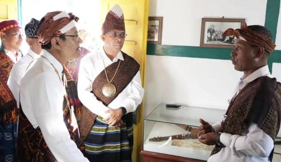 Beberapa pria mengenakan pakaian adat Nusa Tenggara Timur sedang berbincang di dalam ruangan dengan pajangan benda bersejarah.