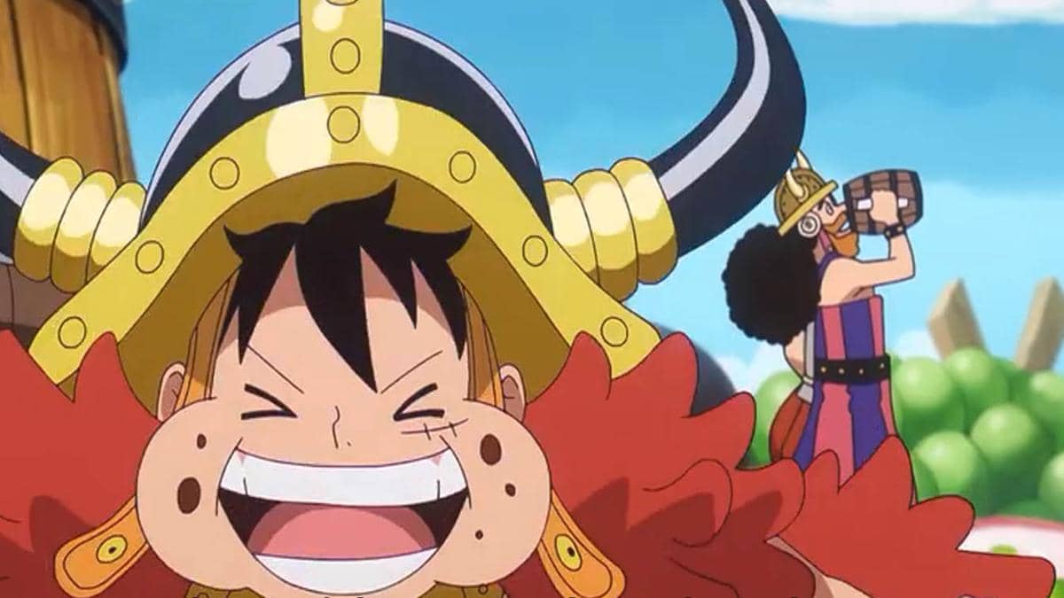 Luffy tersenyum lebar mengenakan helm bertanduk emas sementara salah satu kru Topi Jerami minum dari tong di latar belakang.
