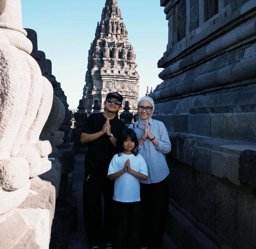 Sebuah keluarga berpose dengan tangan disatukan di antara bangunan batu candi di Yogyakarta dengan latar belakang langit biru cerah.