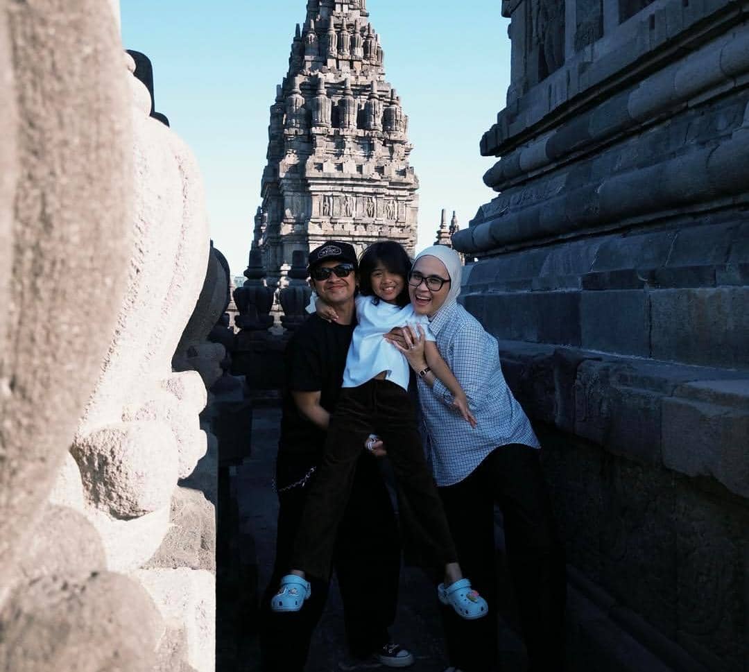 Sebuah keluarga berpose ceria di area Candi Prambanan, Yogyakarta, dengan latar belakang arsitektur batu kuno yang megah.