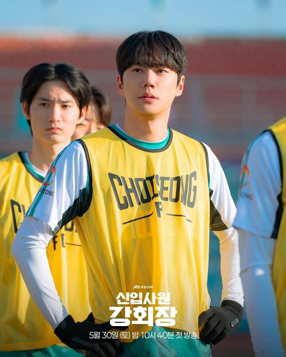 Pemeran drama Reborn Rookie mengenakan rompi latihan kuning bertuliskan Choeoeng F di lapangan dengan latar tribun stadion.