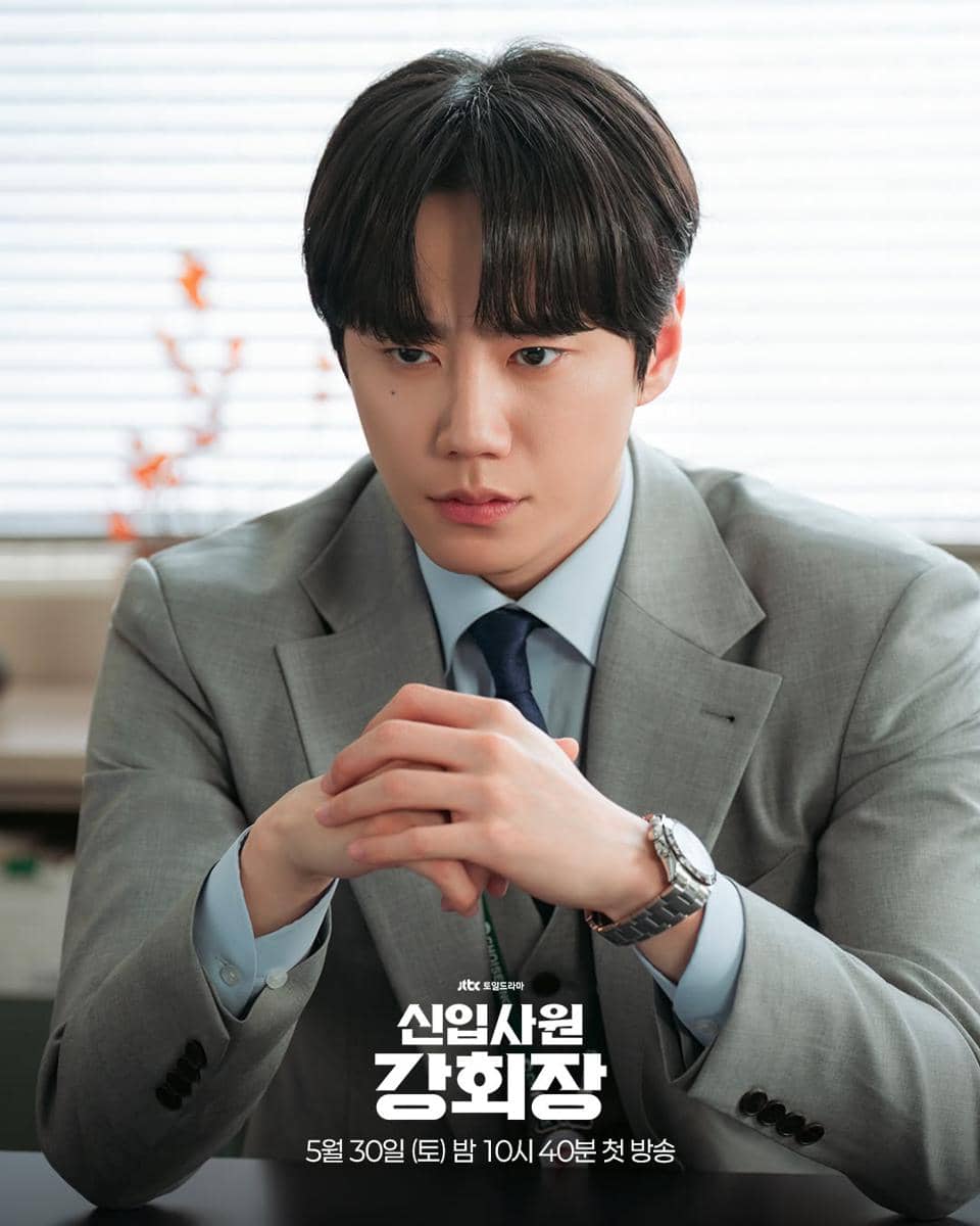 Seorang pria mengenakan setelan jas abu-abu duduk dengan ekspresi serius di meja kantor dalam cuplikan drama Reborn Rookie.